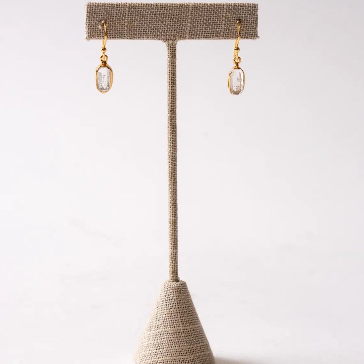 Gold herkimer diamond earrings on a textured beige stand against a white background