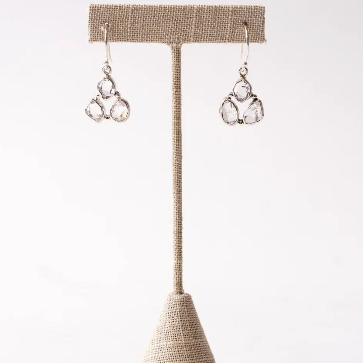 Pair of silver herkimer diamond earrings on a beige earring stand against a white background