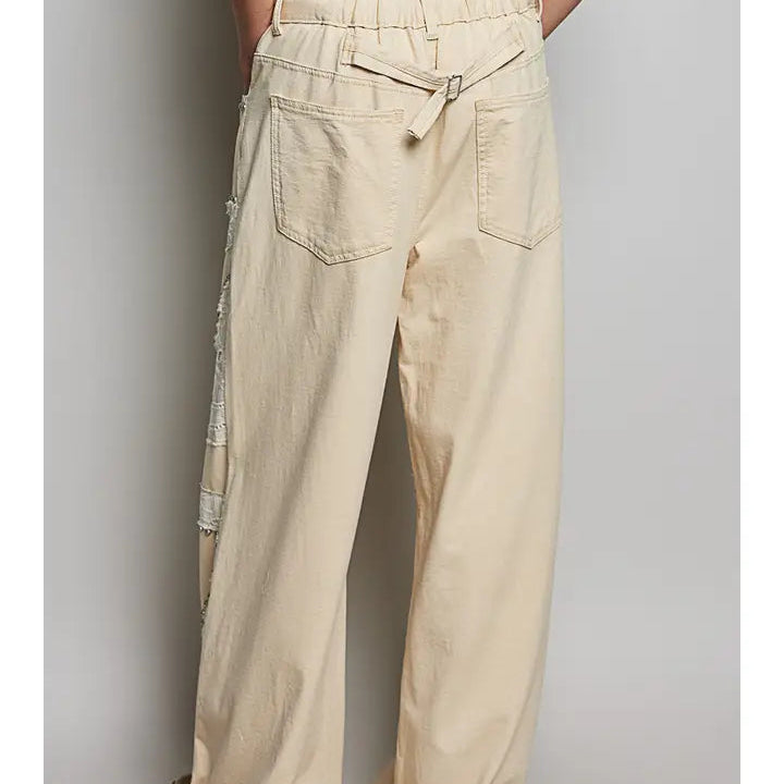 A person wearing wide-leg beige pants with an elastic waistband, side pockets, and a decorative tie detail, shown from the back against a plain light gray studio background.