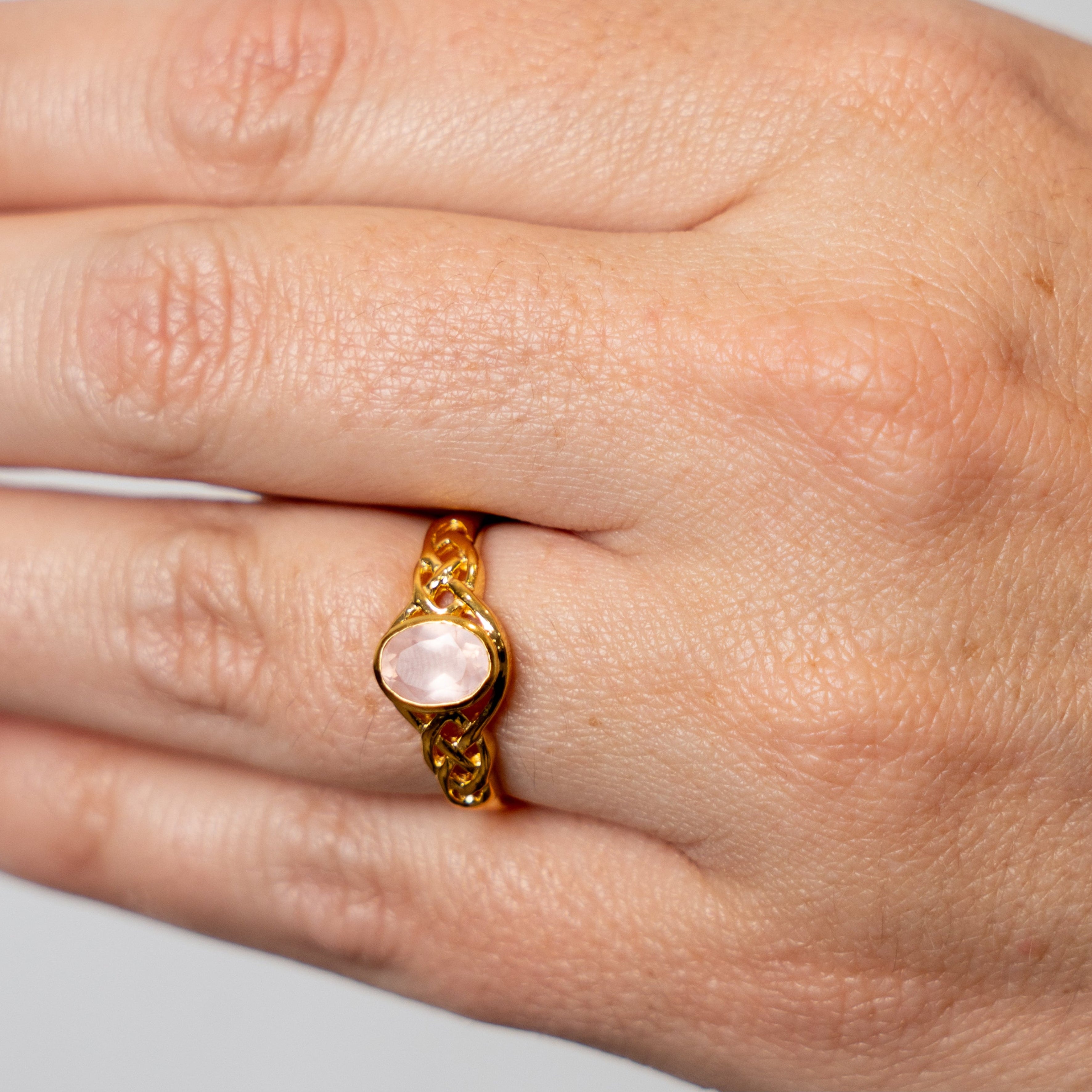 Hand wearing a gold faceted rose quartz ring with a pink gemstone on a light gray background