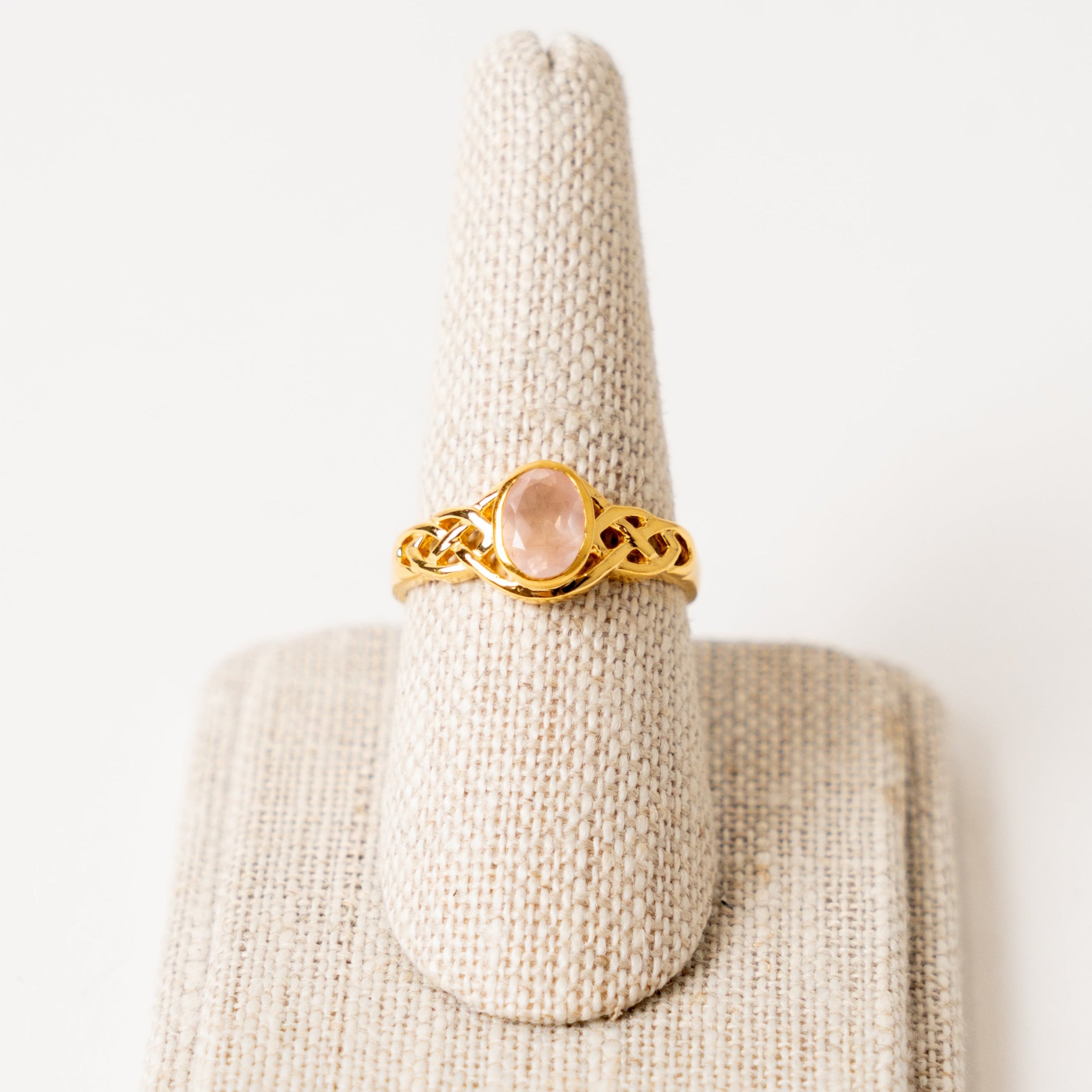 Gold ring with a rose quartz stone on a beige jewelry display stand against a white background