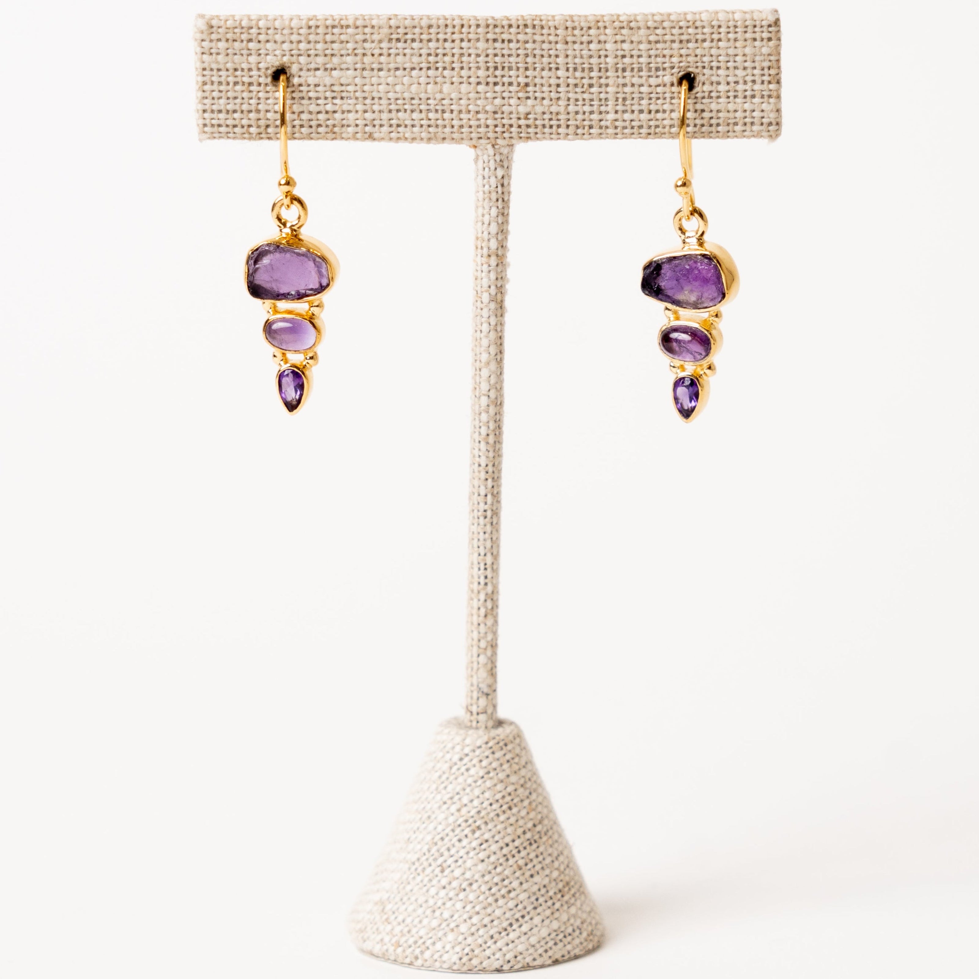 Pair of amethyst earrings on a beige earring stand against a white background
