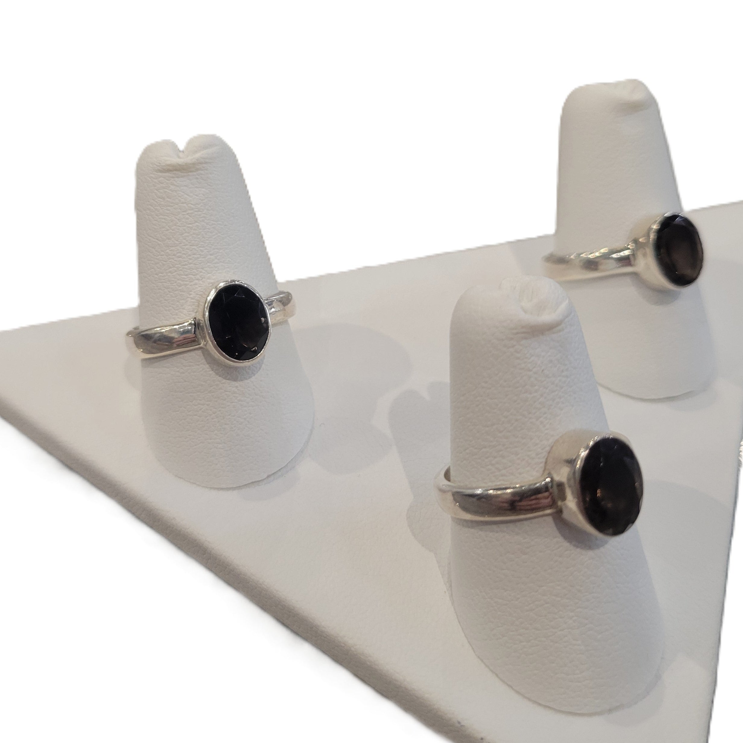 Set of three silver rings with faceted smoky quartz stones on white stands against a white background