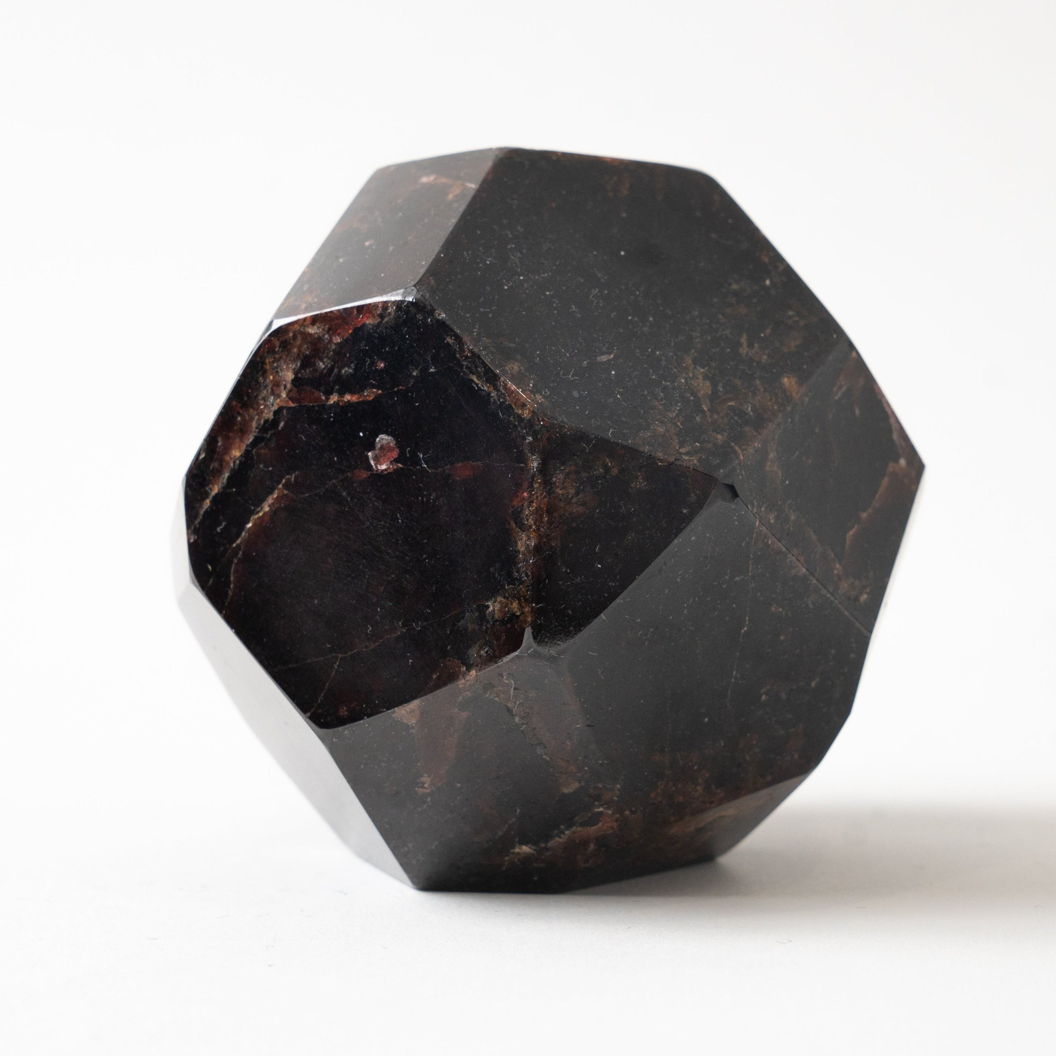 A faceted dark red garnet gemstone specimen on a clean white background.