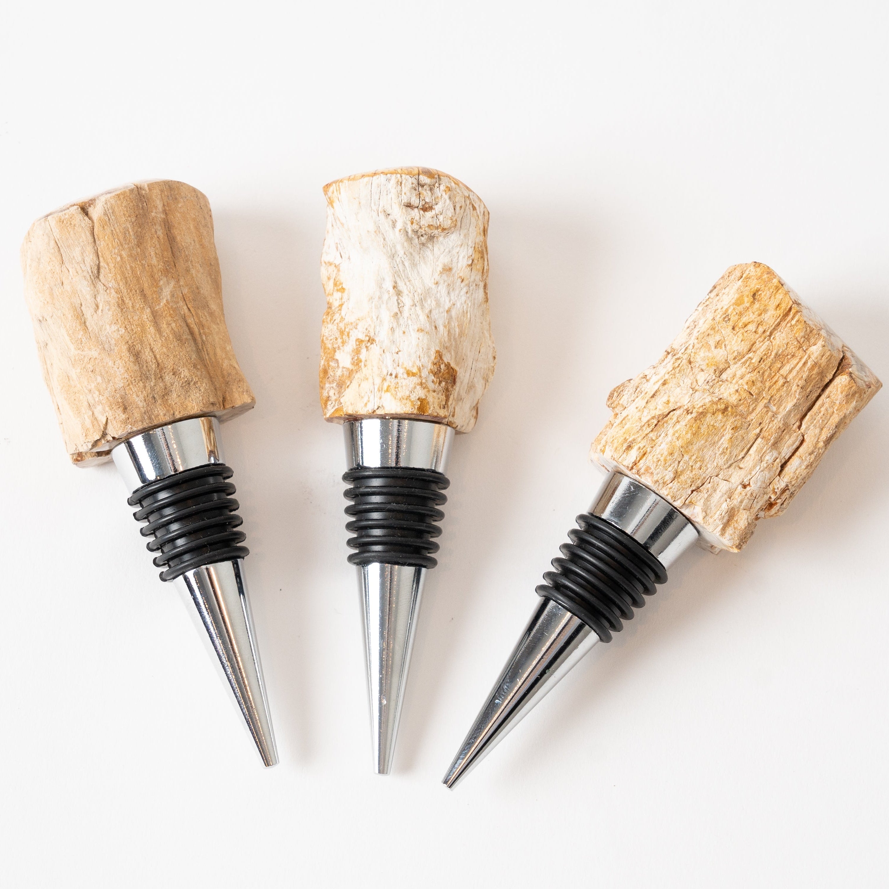 Three petrified wood wine bottle stoppers with natural cork tops on a white background