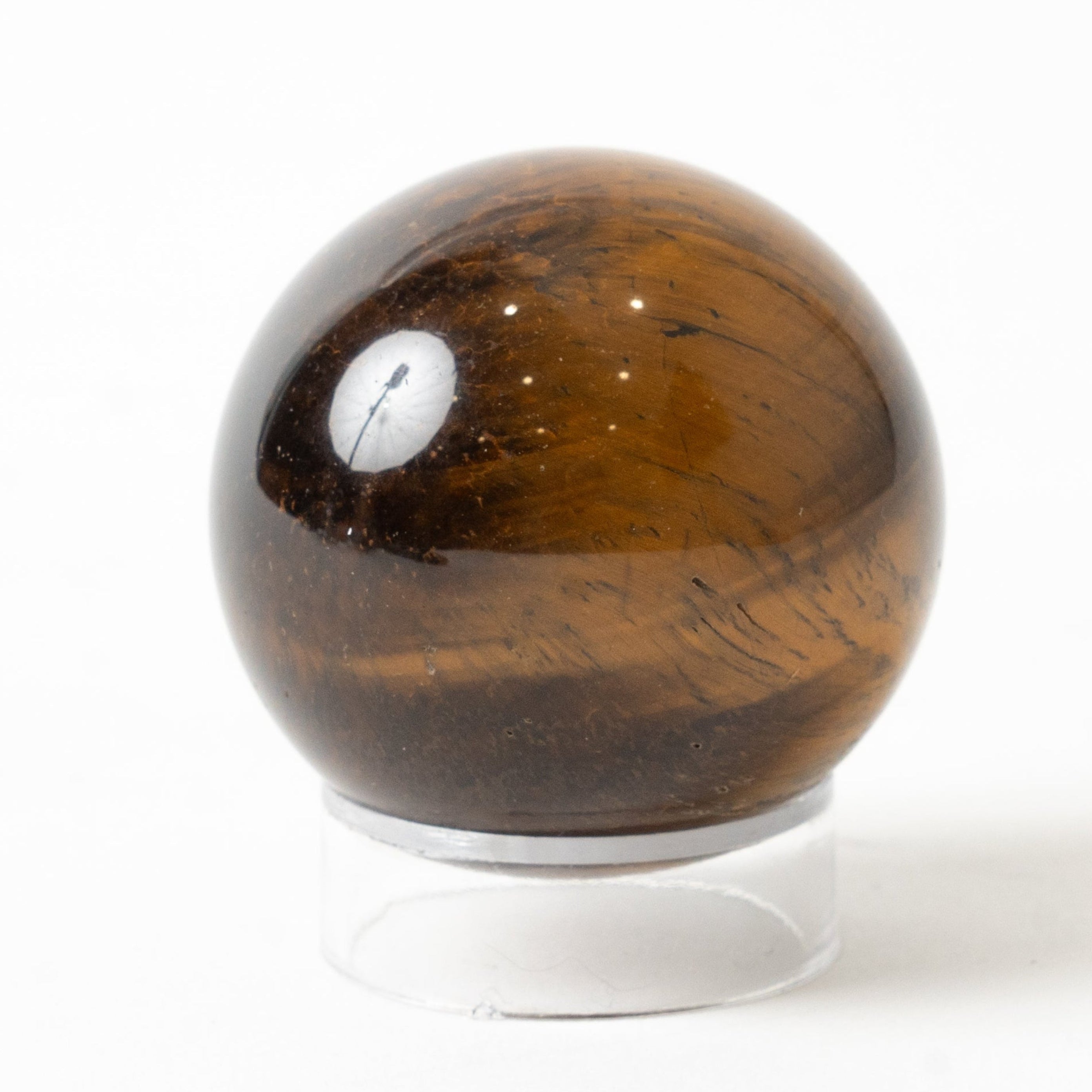Brown tiger's eye crystal ball on a white stand against a white background