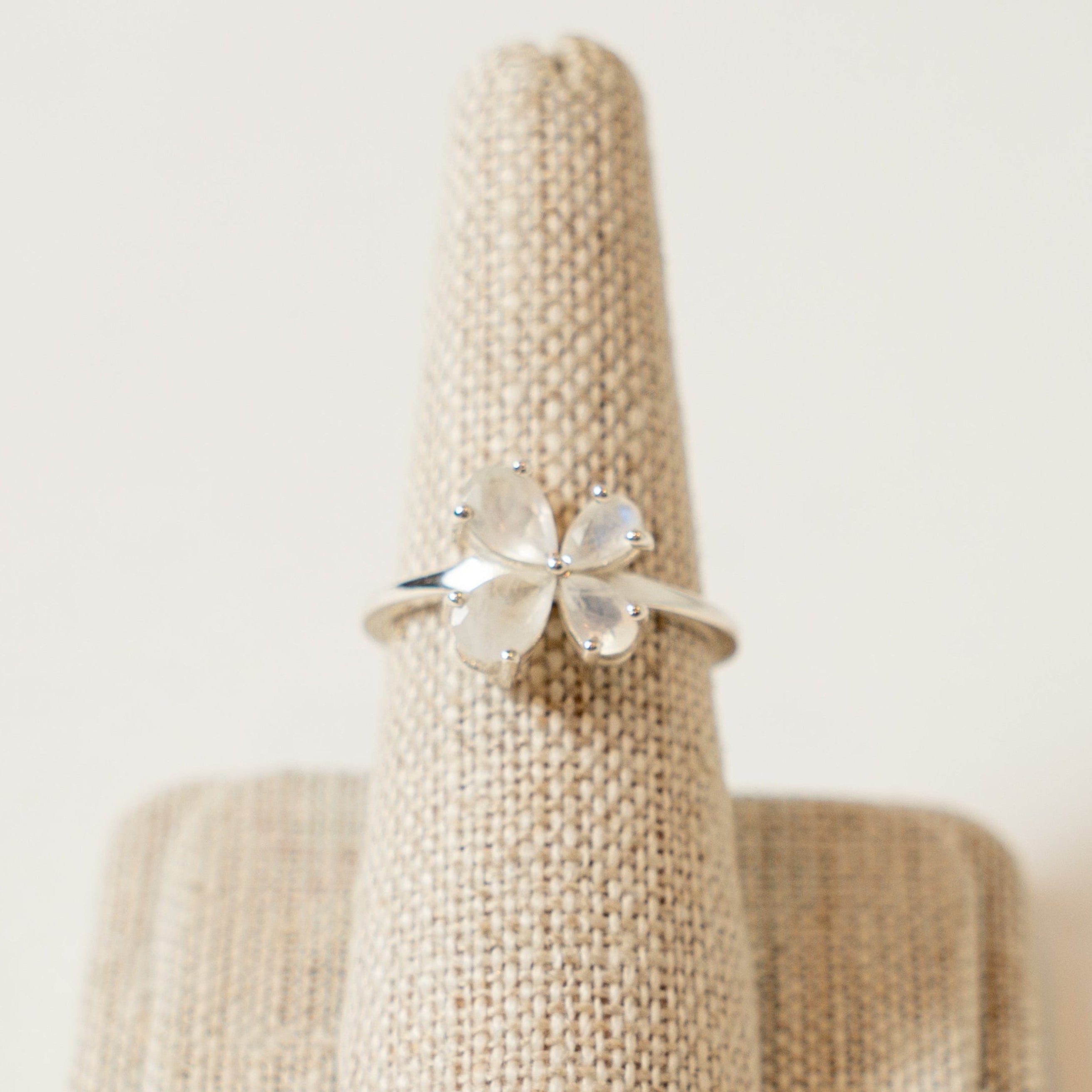 Silver ring with a four-leaf clover design on a textured beige stand against a light background