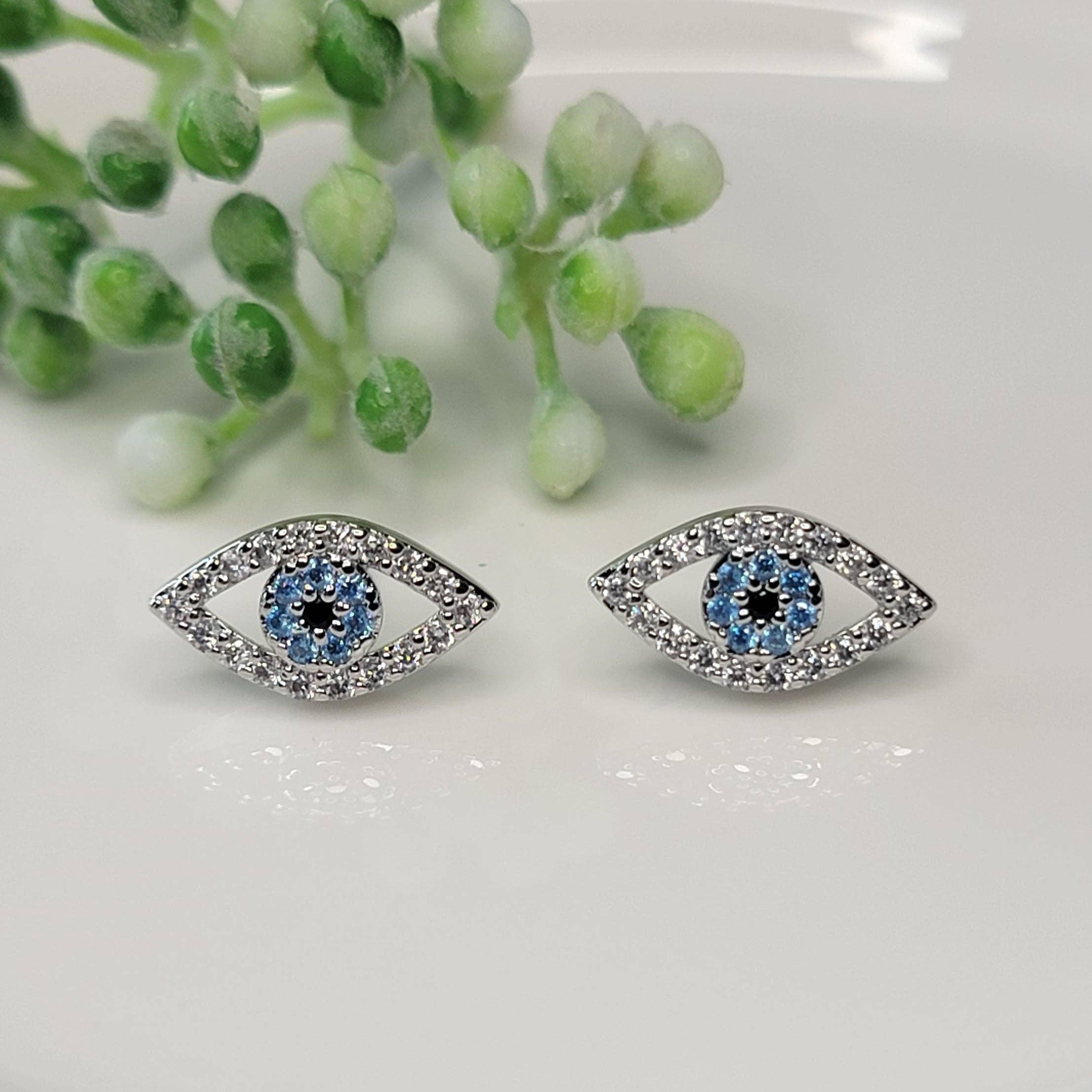 Pair of eye-shaped earrings with blue gemstones on a white surface with greenery.