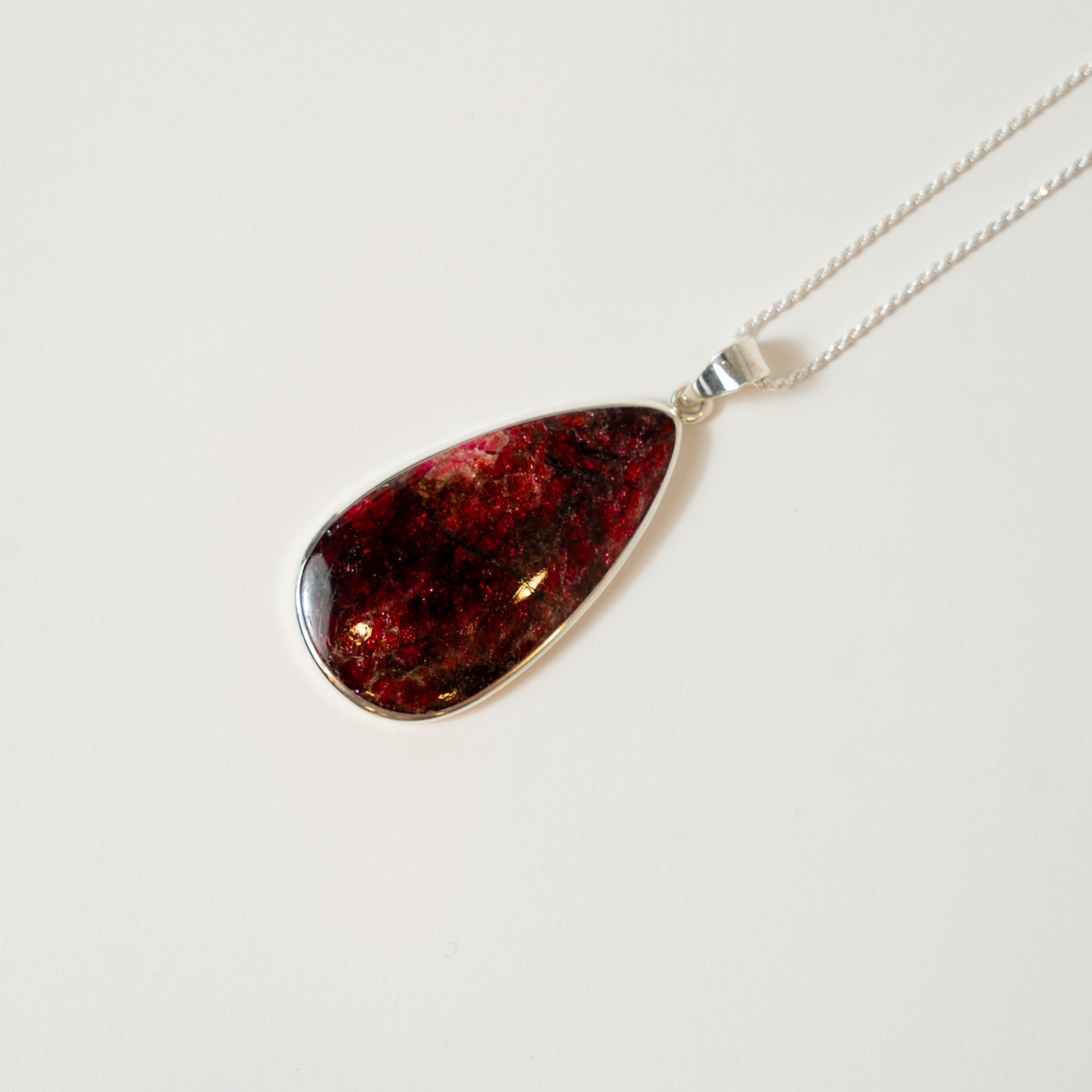 Teardrop-shaped amber pendant on a silver chain against a white background