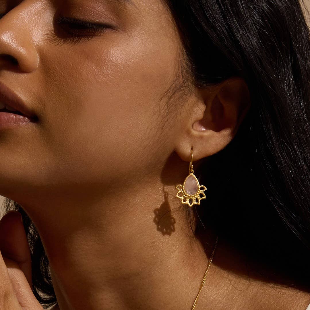 Close-up of a woman wearing gold Rose Quartz Lotus Earrings earrings with a teardrop-shaped gemstone.