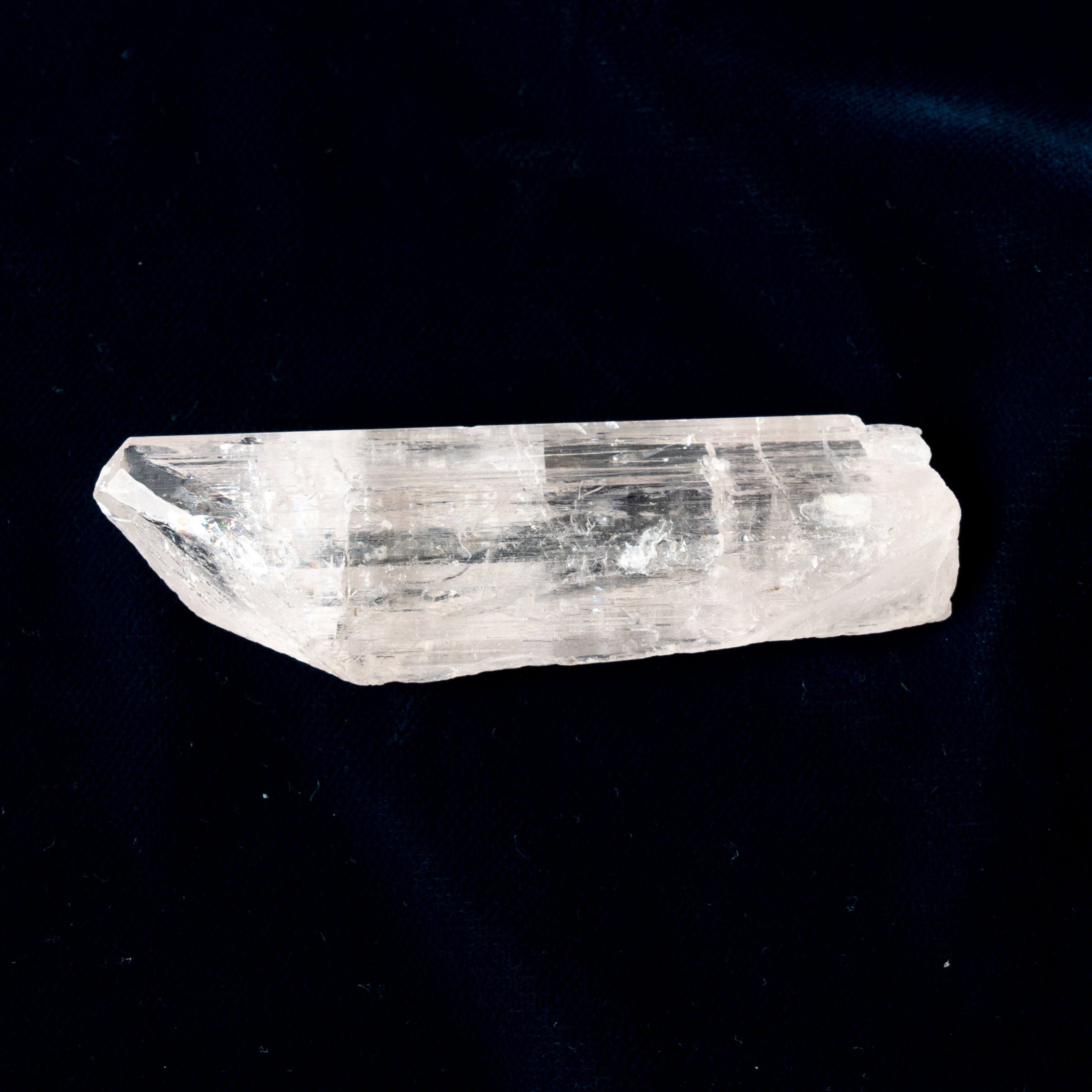 Clear Danburite crystal on a dark blue fabric background