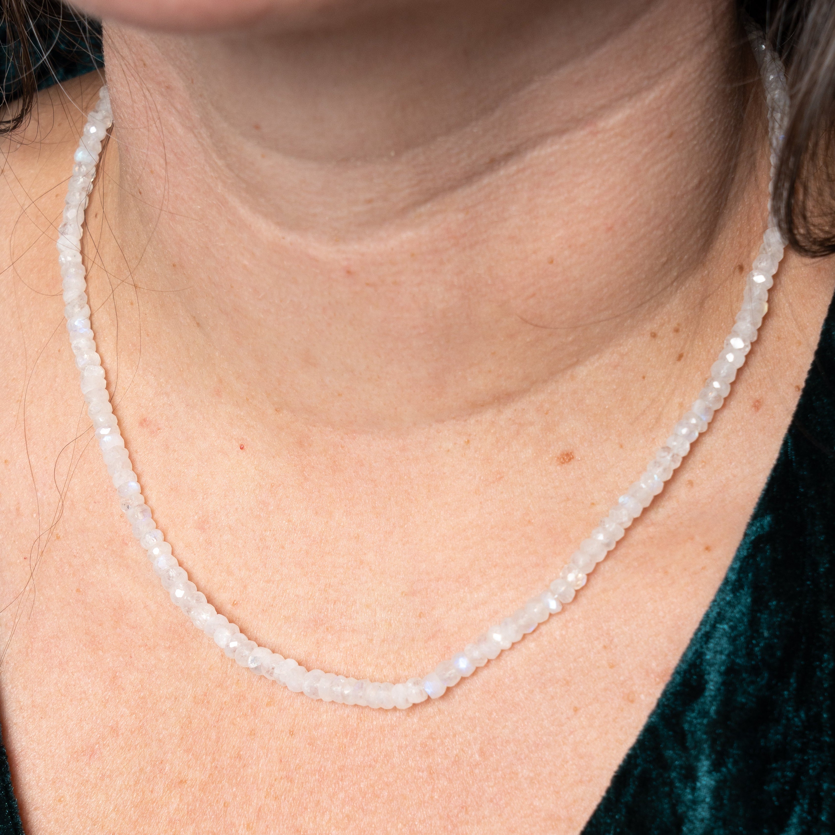 Close-up of a person wearing a delicate pearl necklace with a green velvet garment.