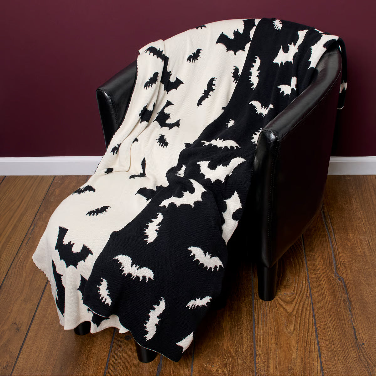 Black and white bat patterned blanket draped over a chair against a maroon wall.