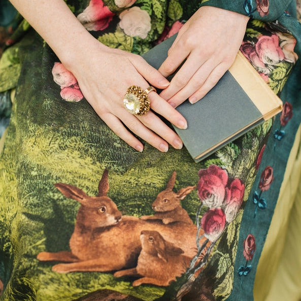 Person wearing a floral dress holding a book, with a close-up of hands and a rabbit illustration on the fabric.
