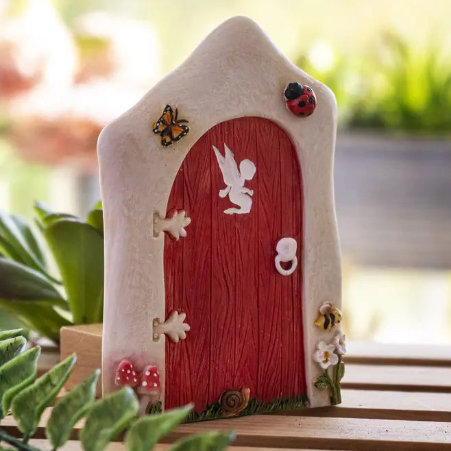 Small fairy house with a red door and decorative elements on a wooden surface.