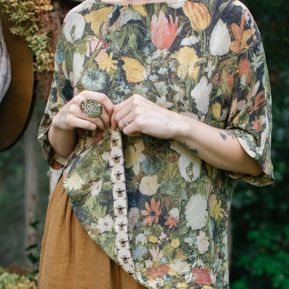 Person wearing a floral blouse and brown pants with a blurred natural background