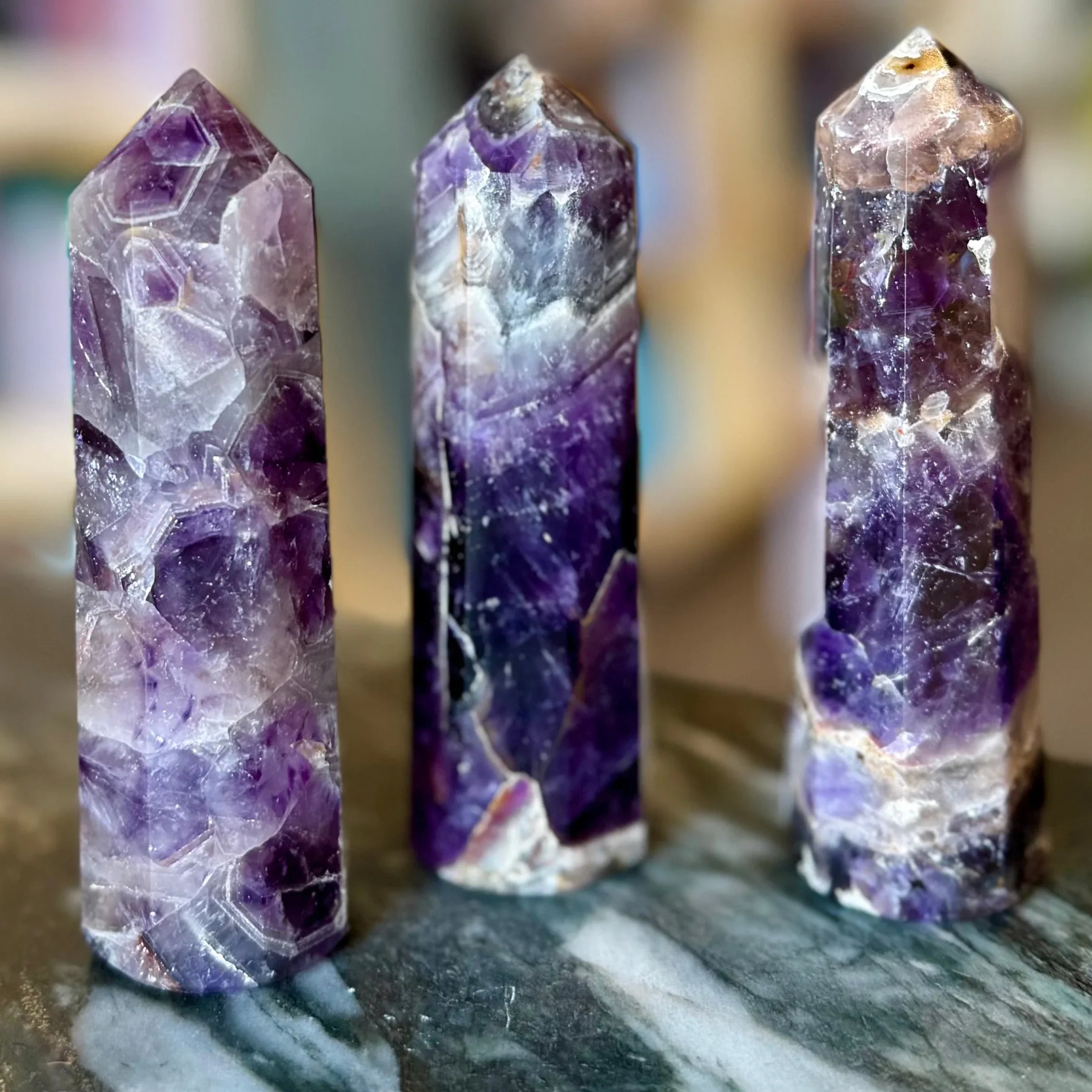 Three amethyst crystal towers on a dark surface with a blurred background