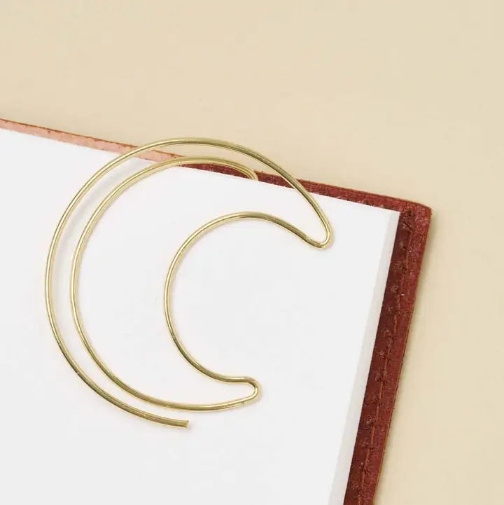 Gold crescent moon-shaped book mark on a white book with a beige background