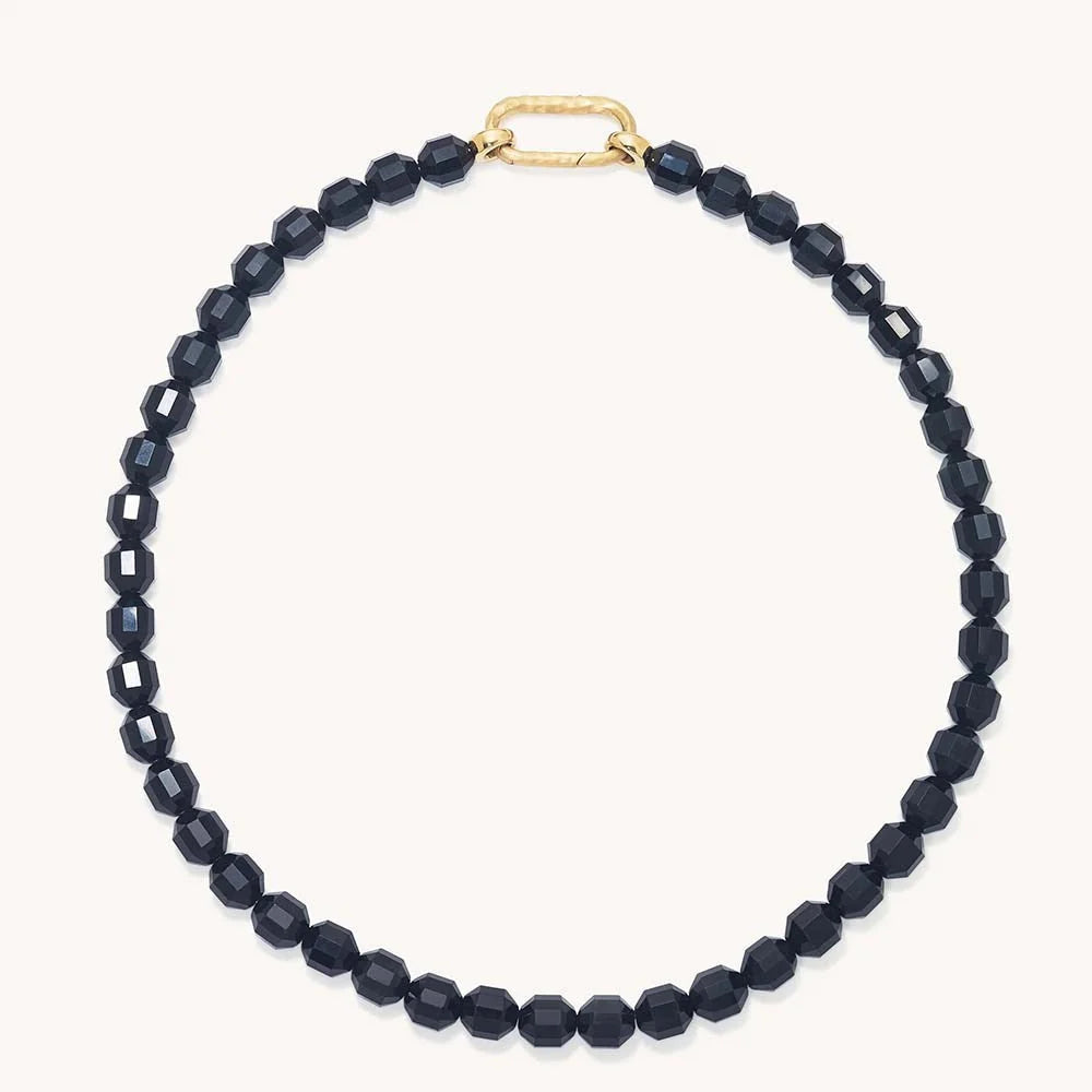 A beaded necklace made of faceted obsidian beads with a gold clasp, displayed on a light cream background.