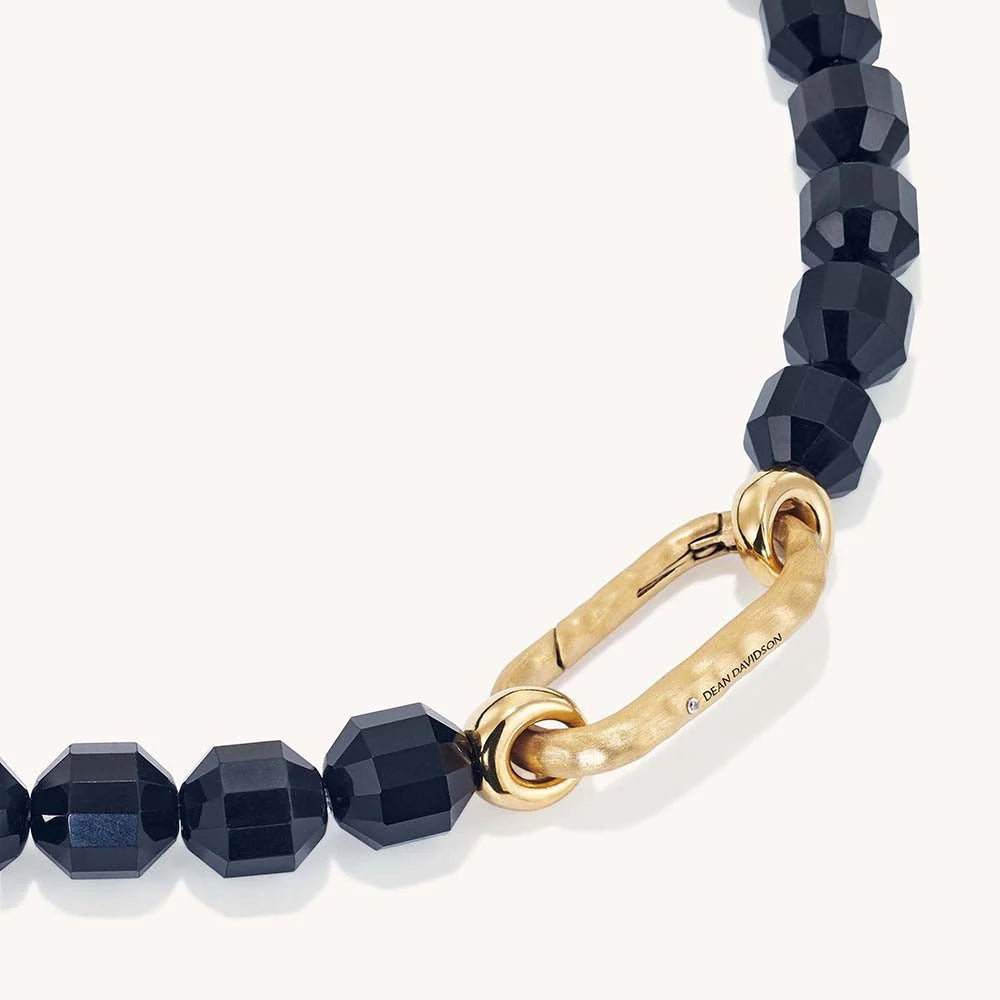 A close-up of a beaded necklace featuring faceted dark obsidian beads and a textured gold clasp with a visible 'Burberrys' brand engraving, set against a clean off-white background.