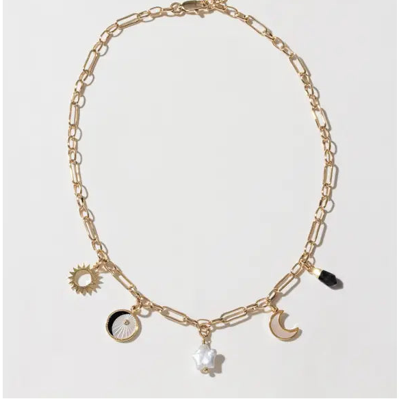 A gold-toned paperclip chain necklace with multiple celestial and abstract charms, including a sun, moon, crescent moon, black and white moon phases, a star, and a small black bead, displayed on a clean white background.