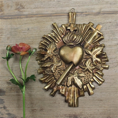 Decorative brass heart-shaped wall hanging on a wooden surface with a single red flower.
