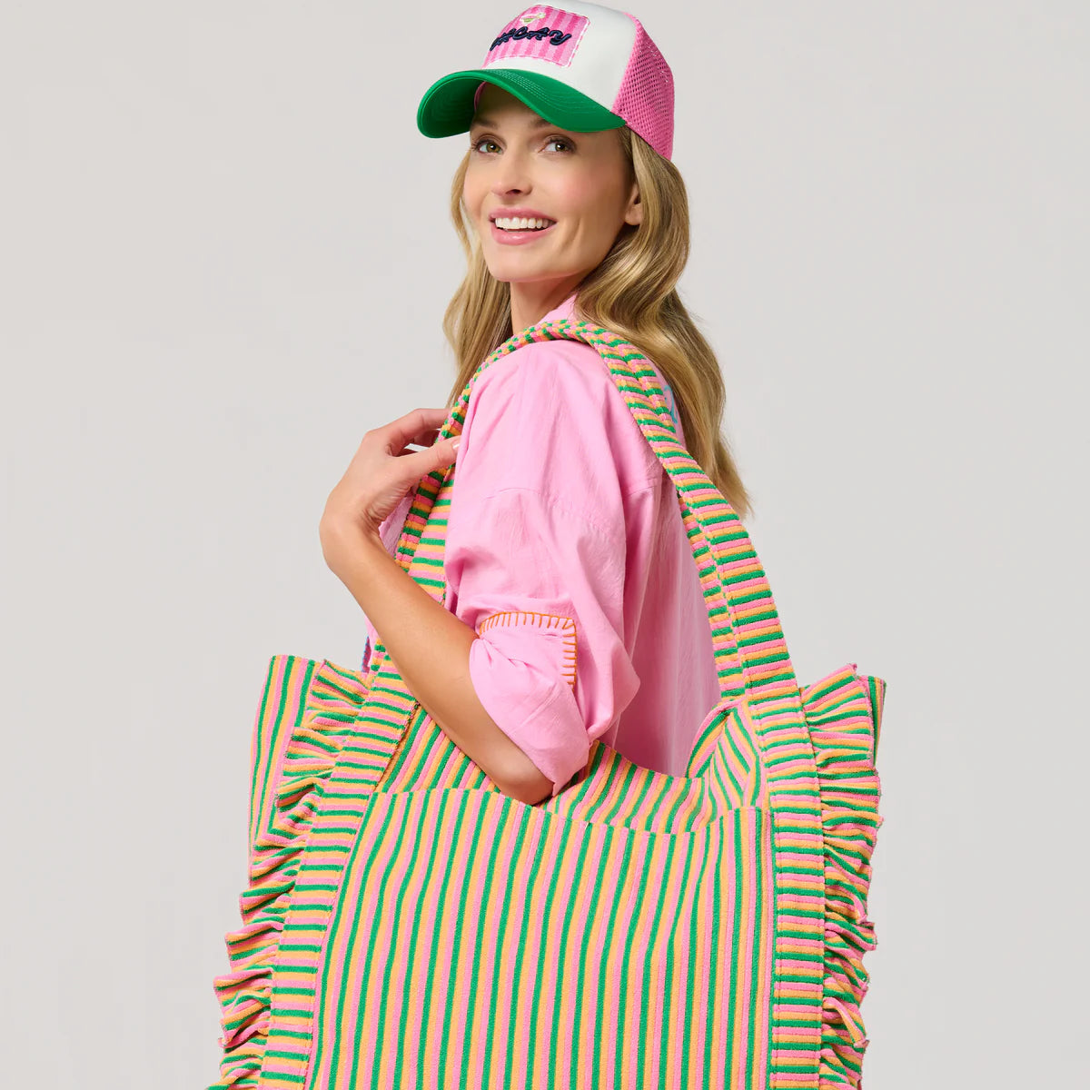 Woman holding a green and pink striped tote bag against a plain background
