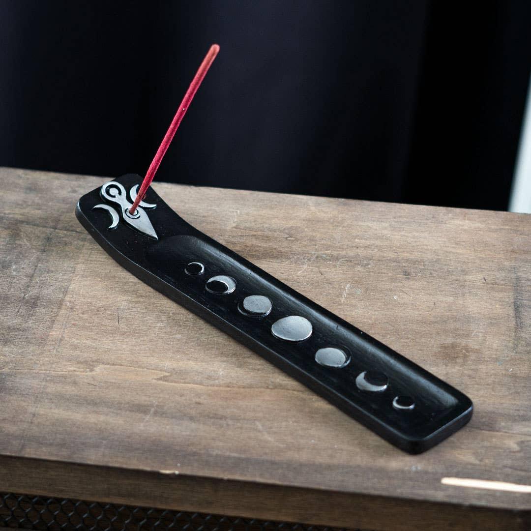 Black incense holder with red incense stick on a wooden surface