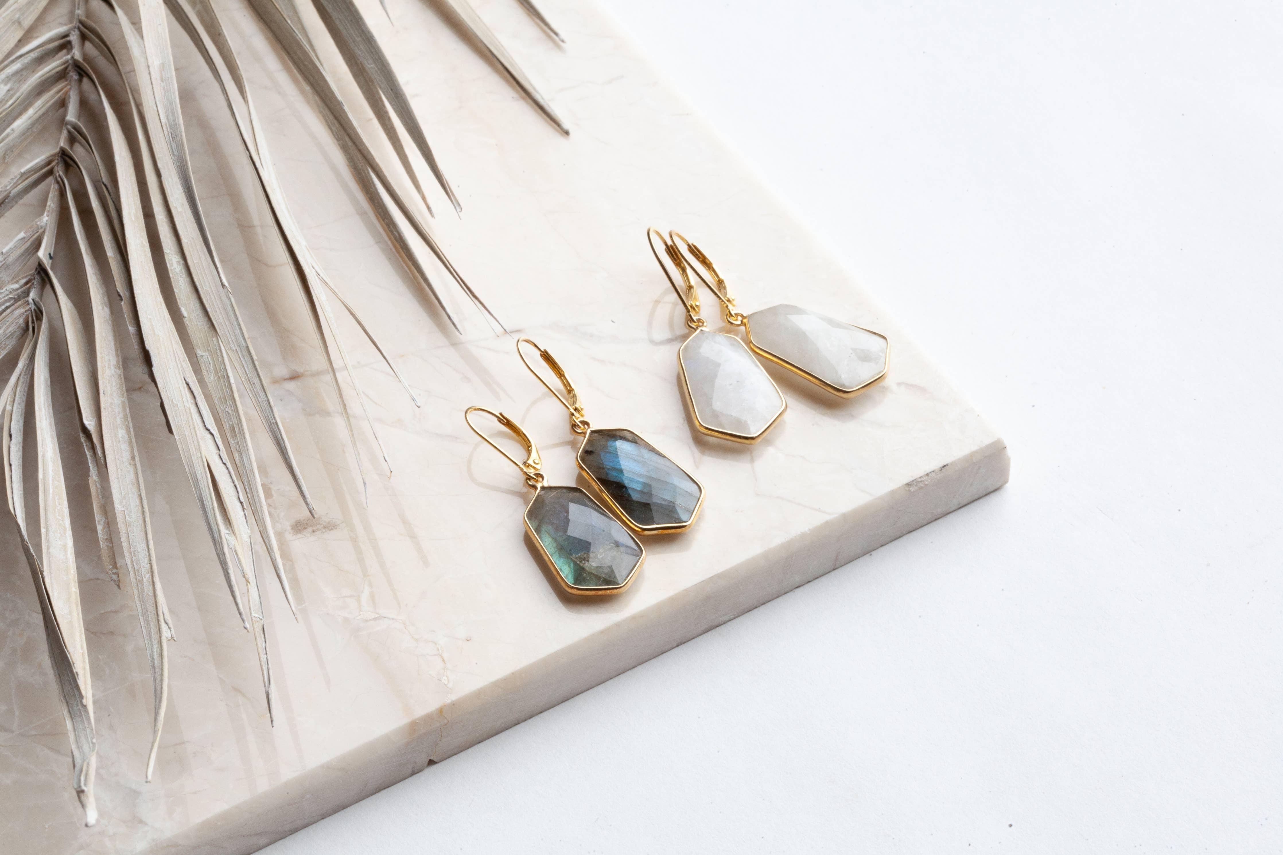 Gold earrings with gemstones on a marble surface