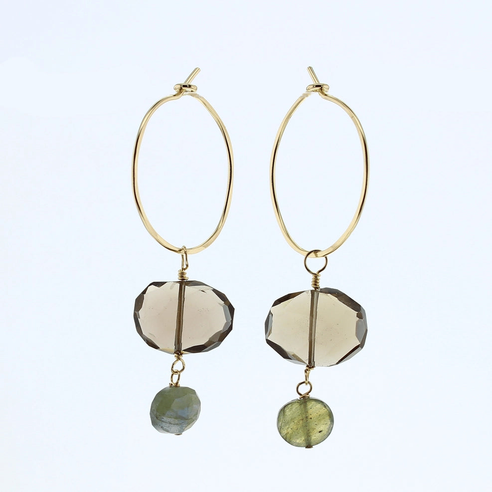 A pair of gold hoop dangle earrings featuring faceted smoky quartz beads and small green labradorite beads, shown against a light blue background.