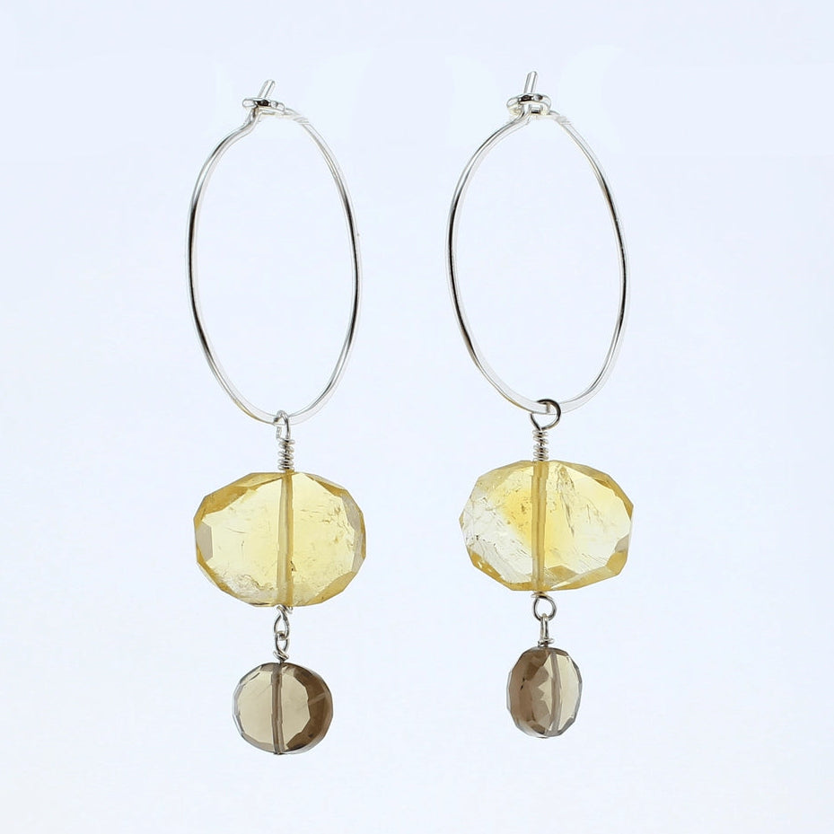 A pair of silver hoop dangle earrings featuring faceted yellow beads and smaller brown smoky beads, shown against a plain white background.