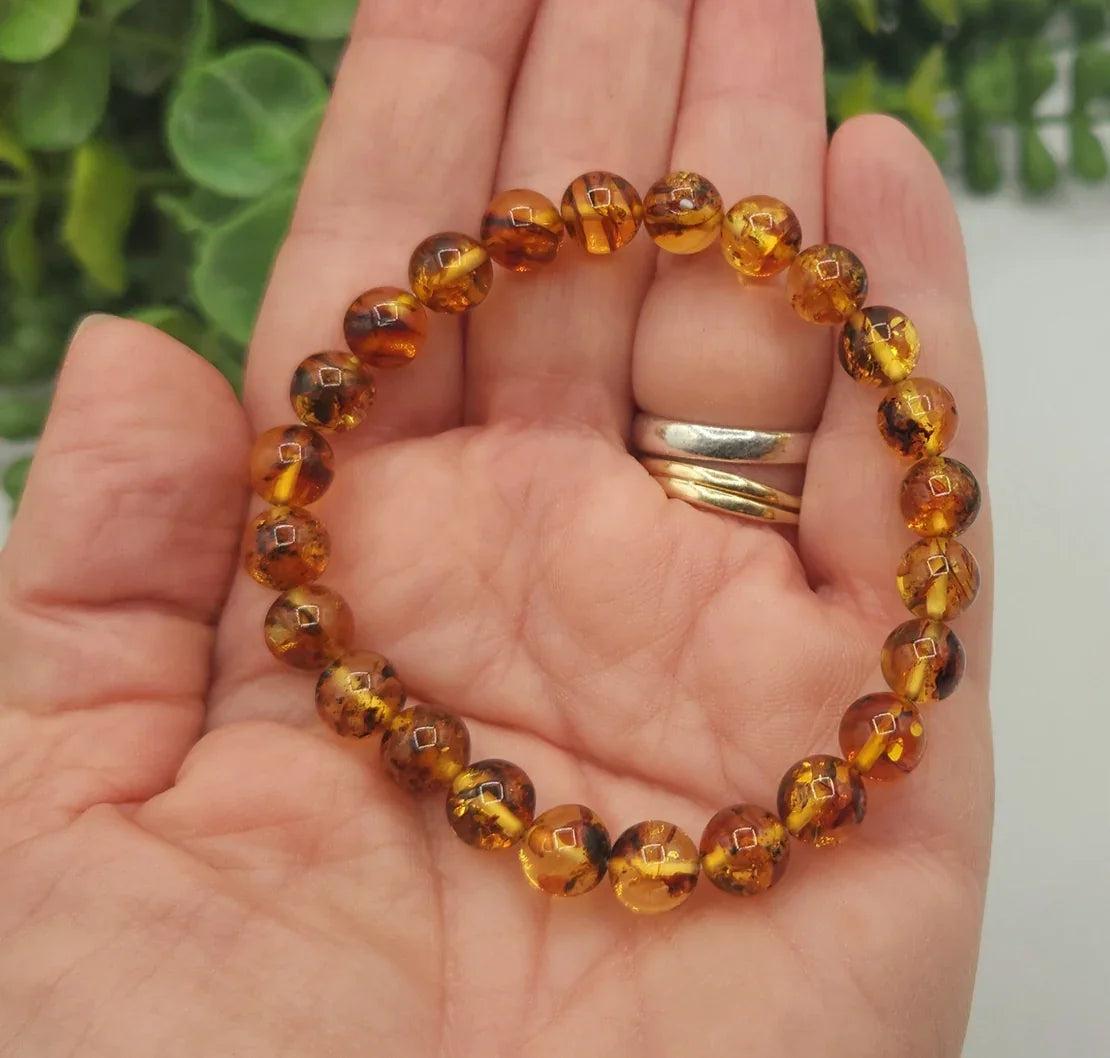 Hand holding a bracelet with amber beads against a blurred green background