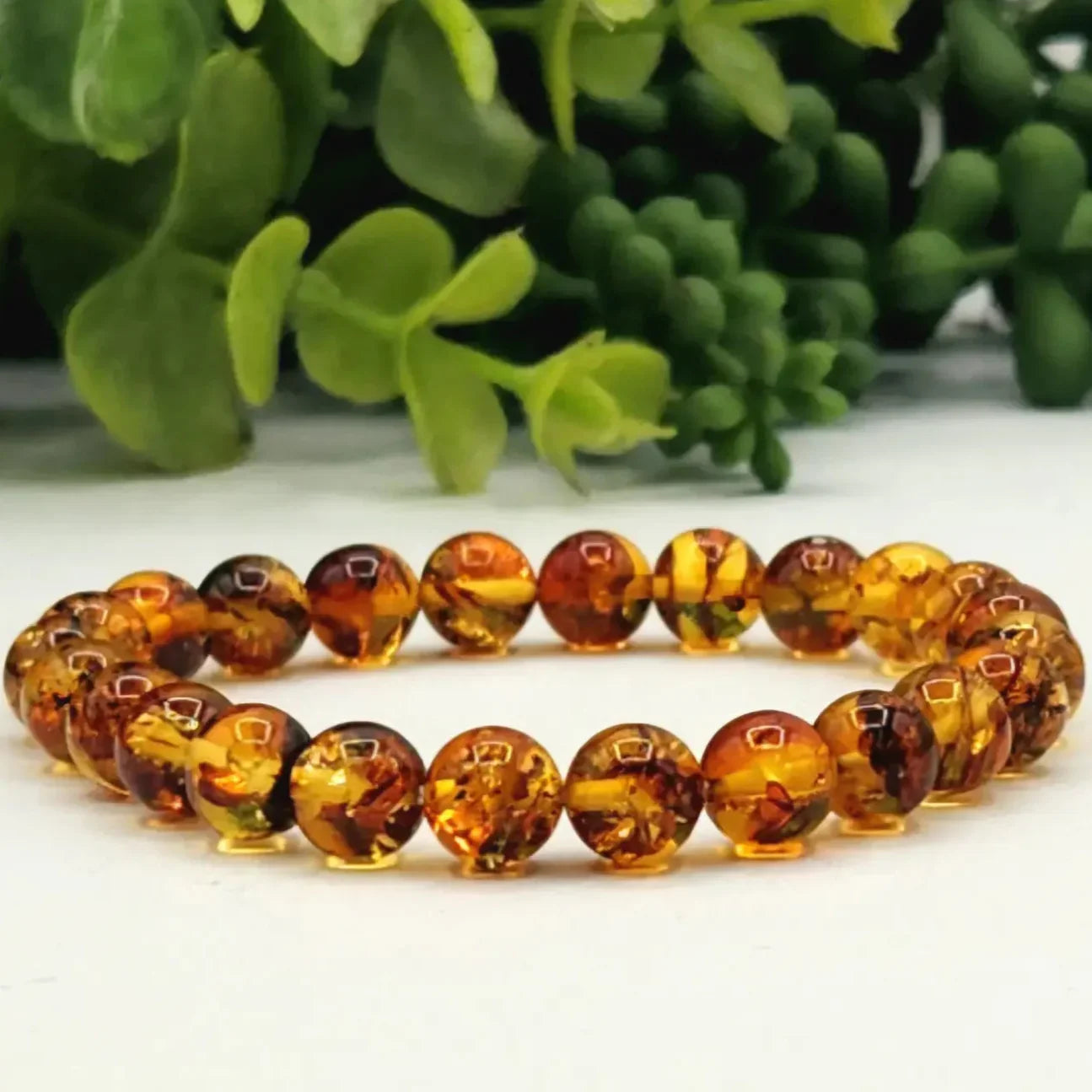 Amber beaded bracelet on a white surface with green leaves in the background