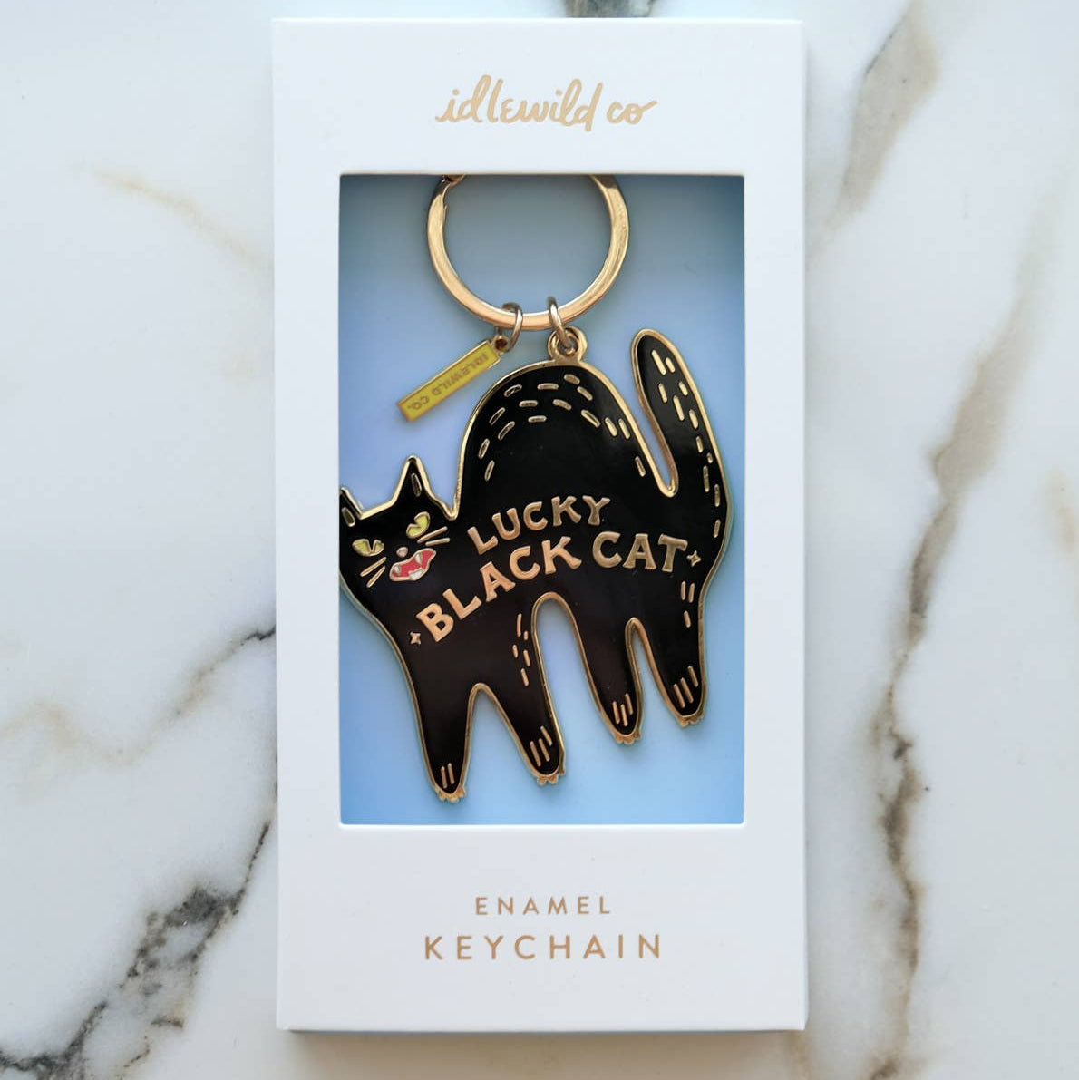 Black cat enamel keychain in packaging on a marble surface