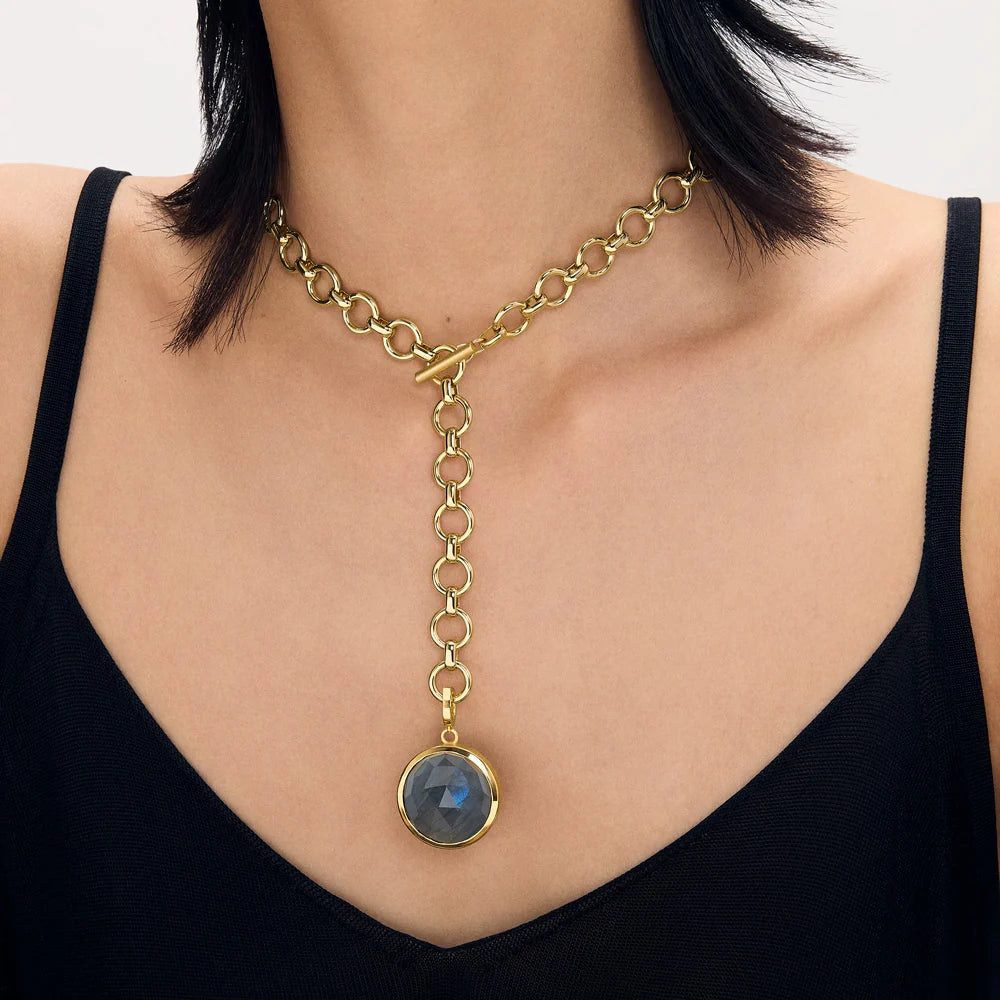 A gold-toned Y-necklace with a toggle clasp and a circular deep blue labradorite pendant, shown worn on a model's neck over a black top.