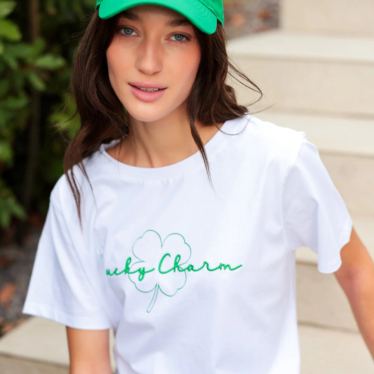 Person wearing a white t-shirt and green cap with 'Lucky Charm' text outdoors.
