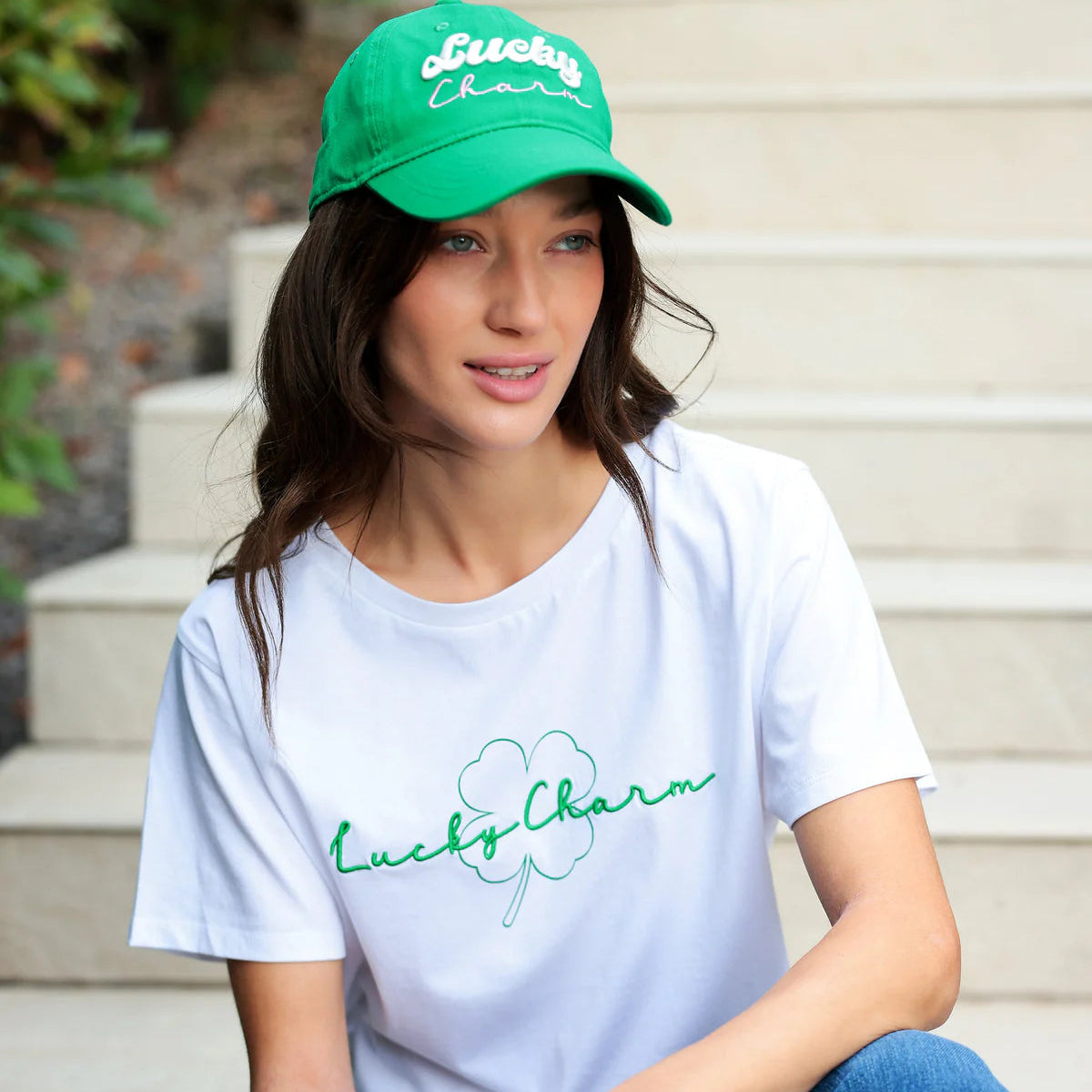 Woman wearing a white t-shirt and green cap with 'Lucky Charm' branding outdoors.