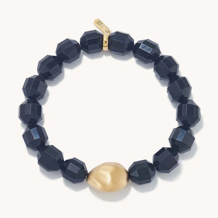 A beaded bracelet featuring faceted dark navy blue beads and one prominent matte gold accent bead, displayed on a clean off-white background.