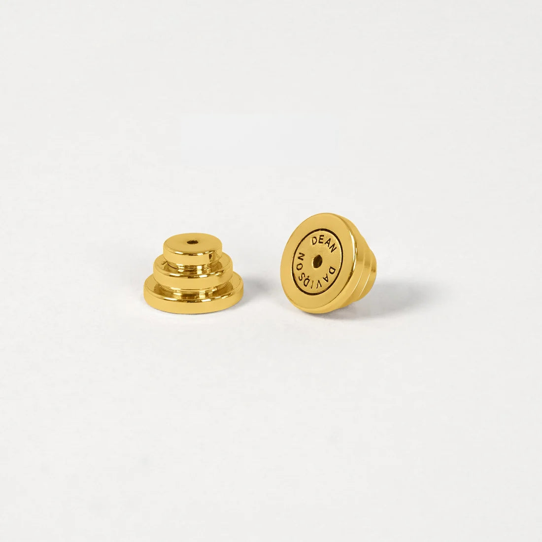 Two small gold metal earbud tips, one showing the layered stem side and the other showing the flat circular end