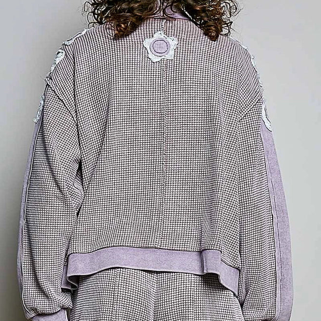 A person shown from the back wearing a matching gray and white houndstooth tracksuit with solid lavender-gray ribbed trim and a circular patch on the back collar, against a plain light gray background.