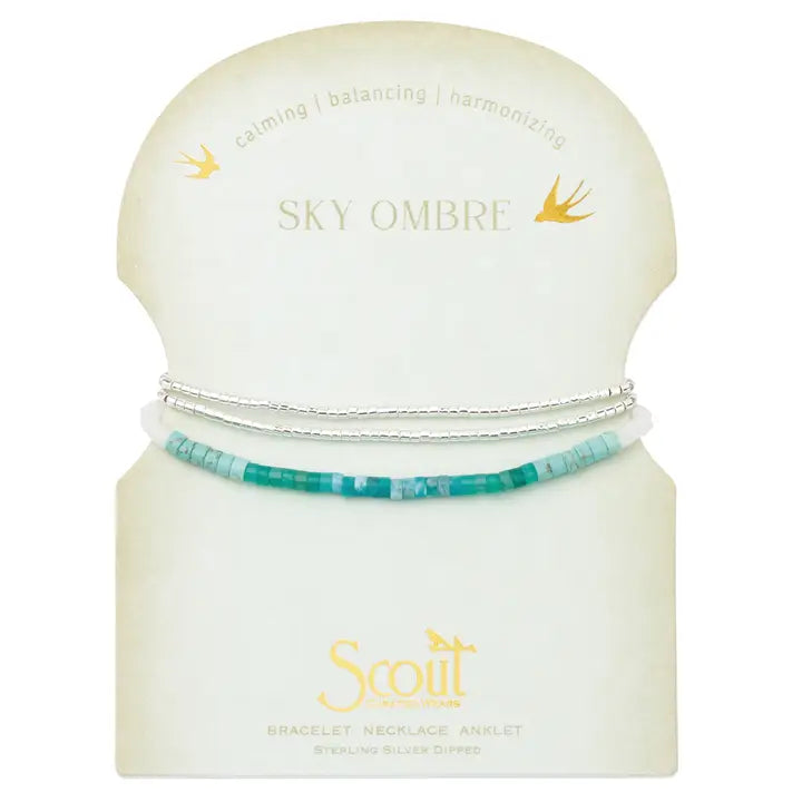 A set of three beaded bracelets displayed on a cream-colored Scott brand card. The bracelets include a silver chain, a silver beaded bracelet with light blue and white beads, and a turquoise-blue beaded bracelet.