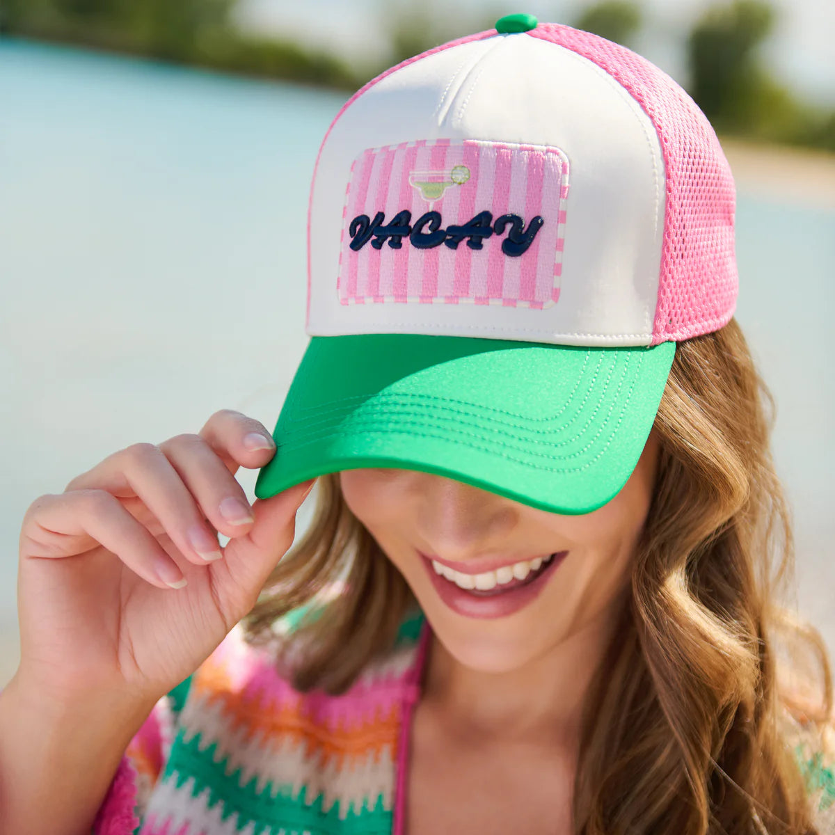Woman wearing a colorful cap with 'Vacay' on it, smiling outdoors.