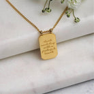 Gold necklace with a pendant on a marble surface with flowers in the background