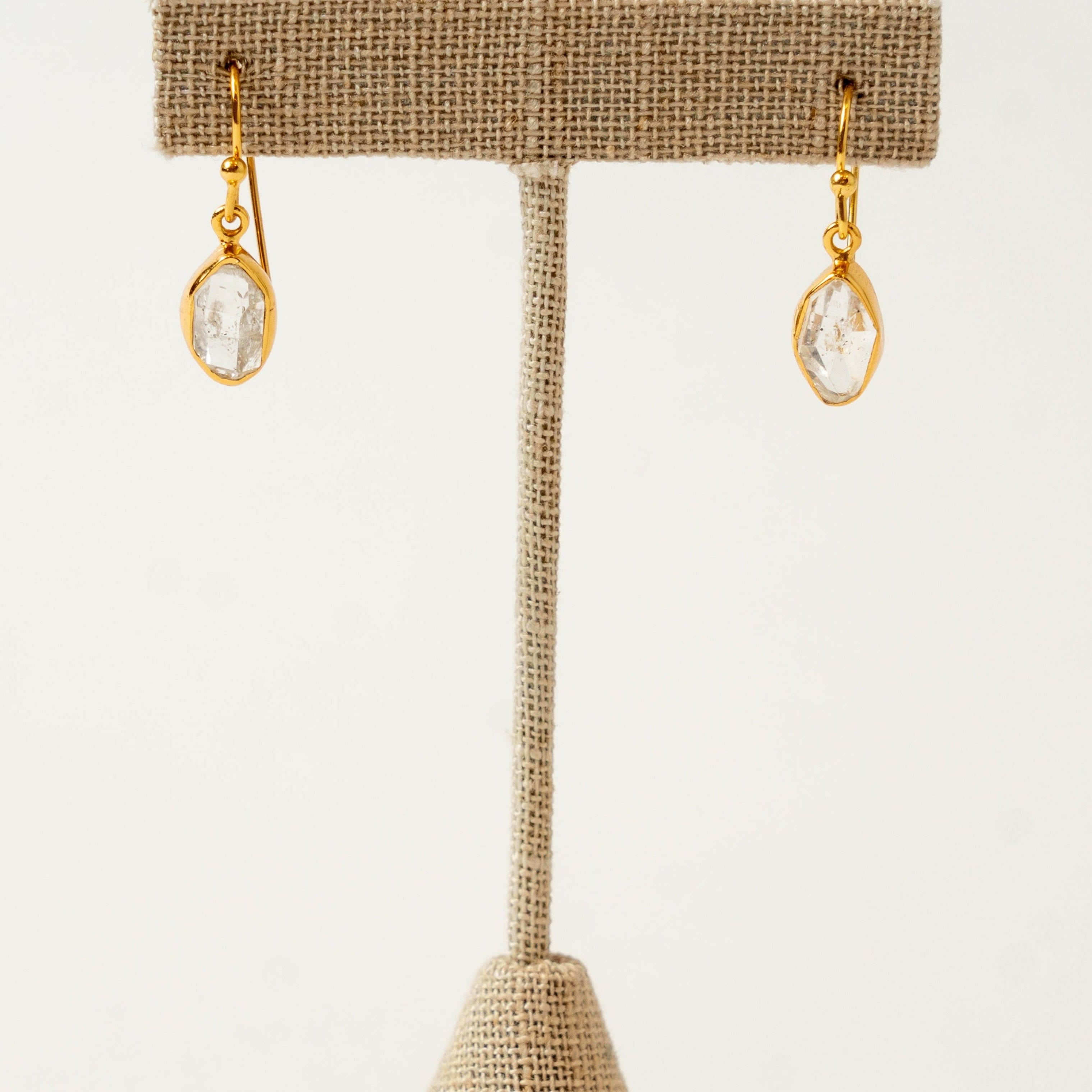 Gold herkimer diamond earrings on a beige jewelry stand against a white background