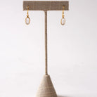 Gold herkimer diamond earrings on a textured beige stand against a white background