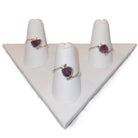Three rings with heart-shaped gemstones on white stands against a white background