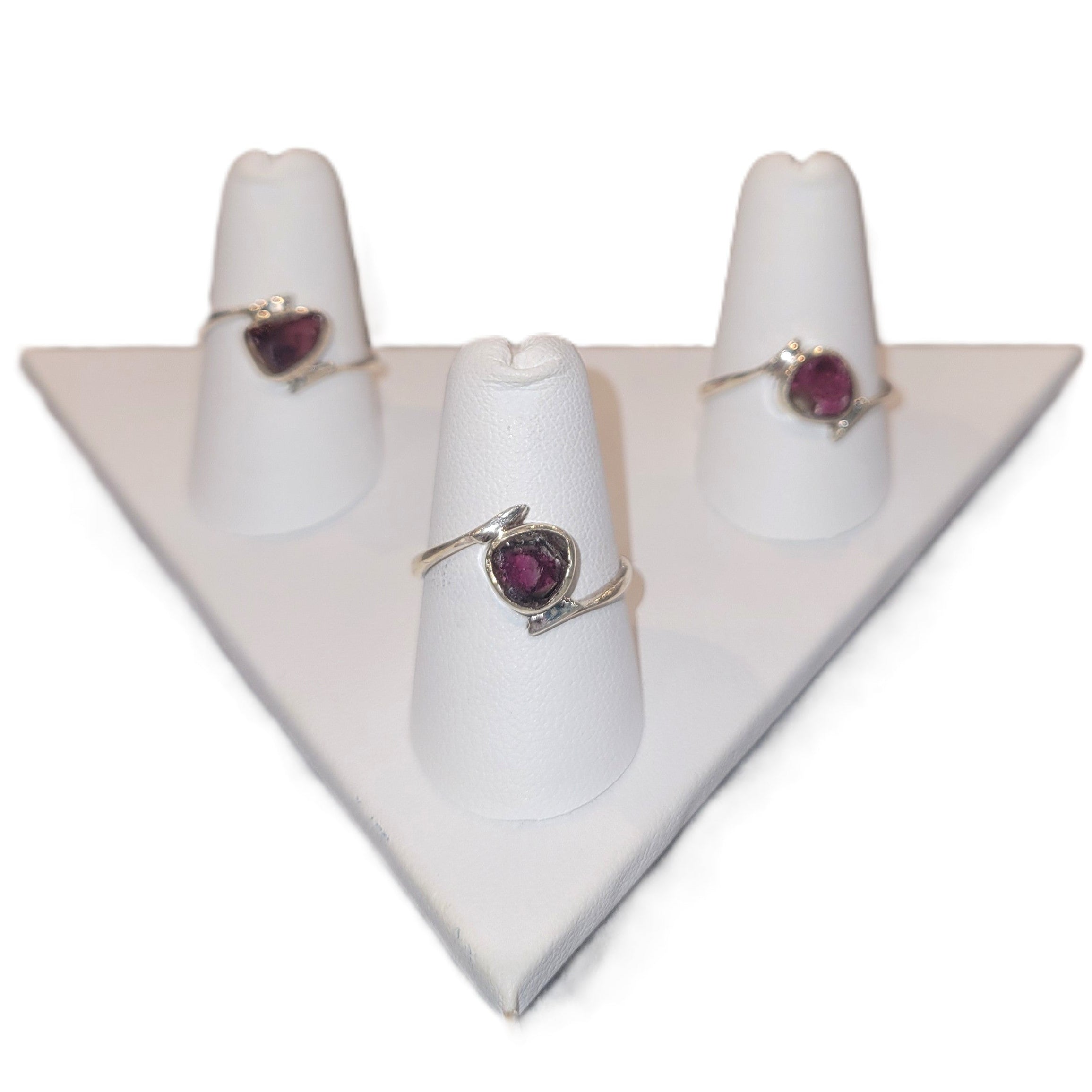 Three rings with heart-shaped gemstones on white stands against a white background
