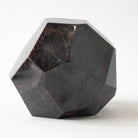 A faceted geometric garnet crystal sculpture made of polished dark stone, showing natural marbling with brown and black tones, set against a plain white background.