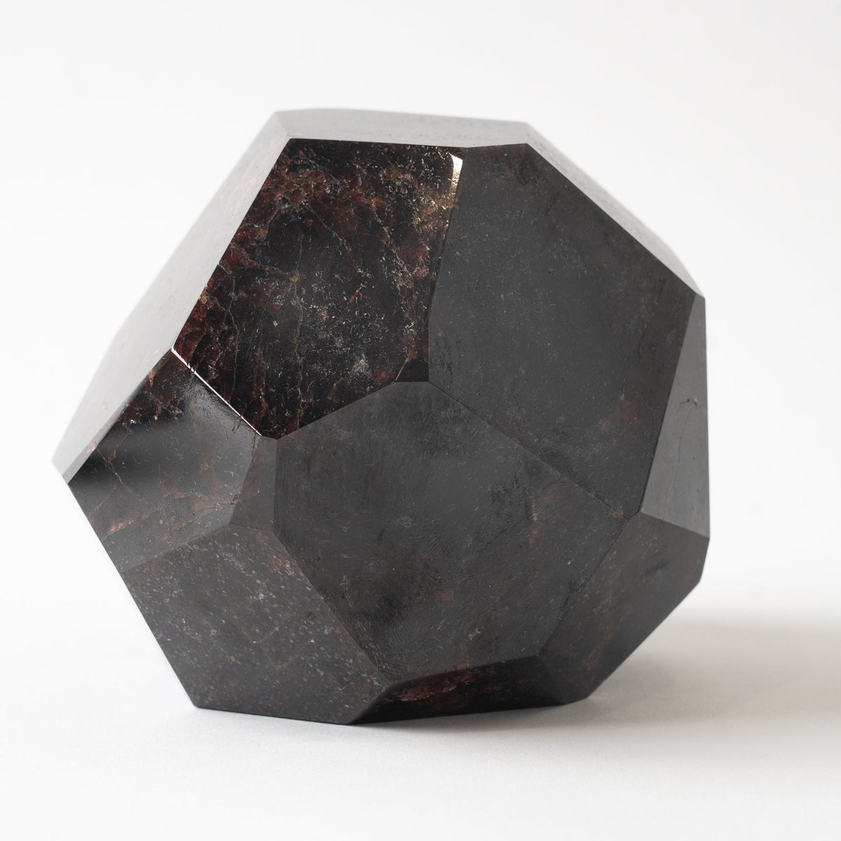 A faceted geometric garnet crystal sculpture made of polished dark stone, showing natural marbling with brown and black tones, set against a plain white background.