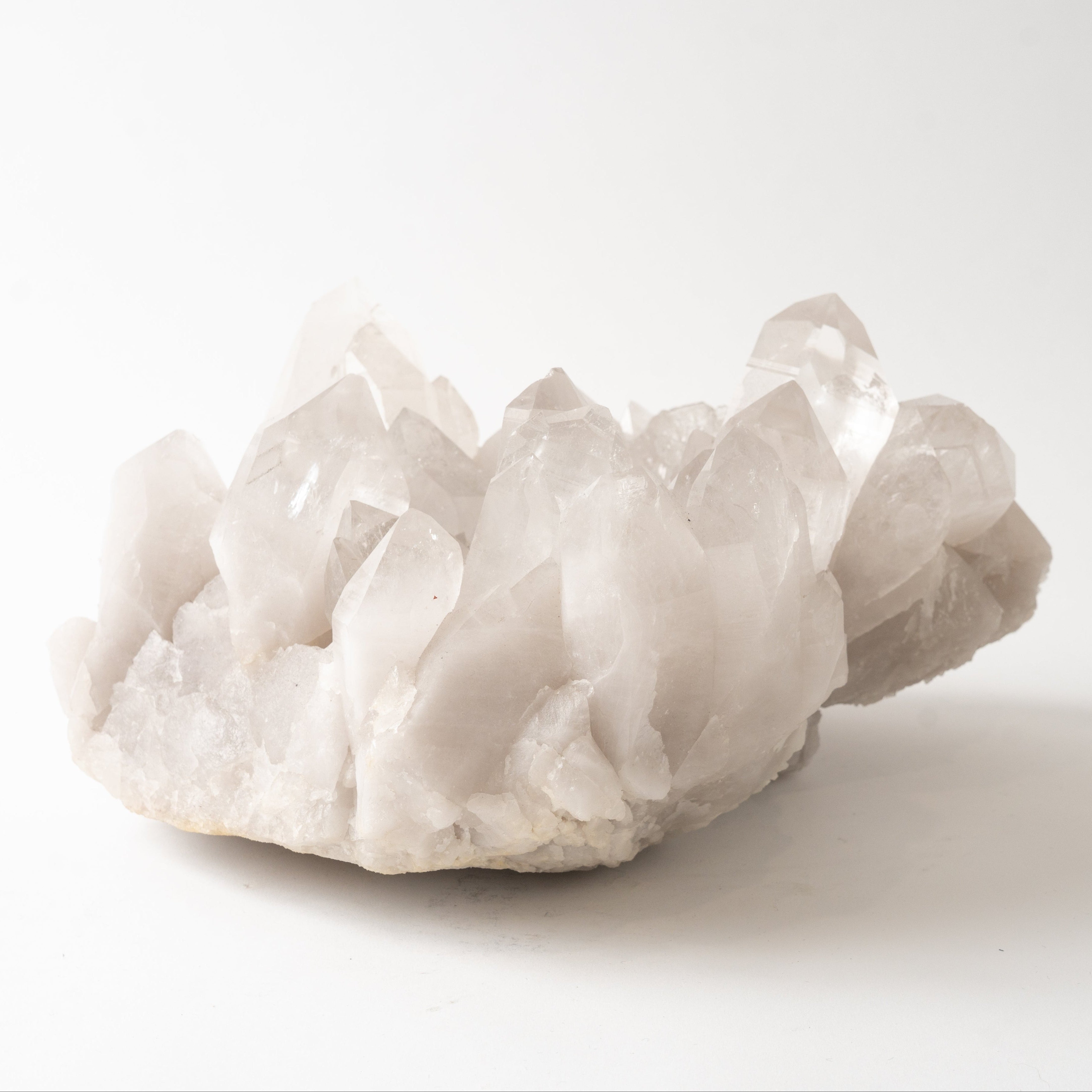A natural quartz crystal cluster with sharp, translucent points resting on a light gray stone base, photographed against a seamless white background.